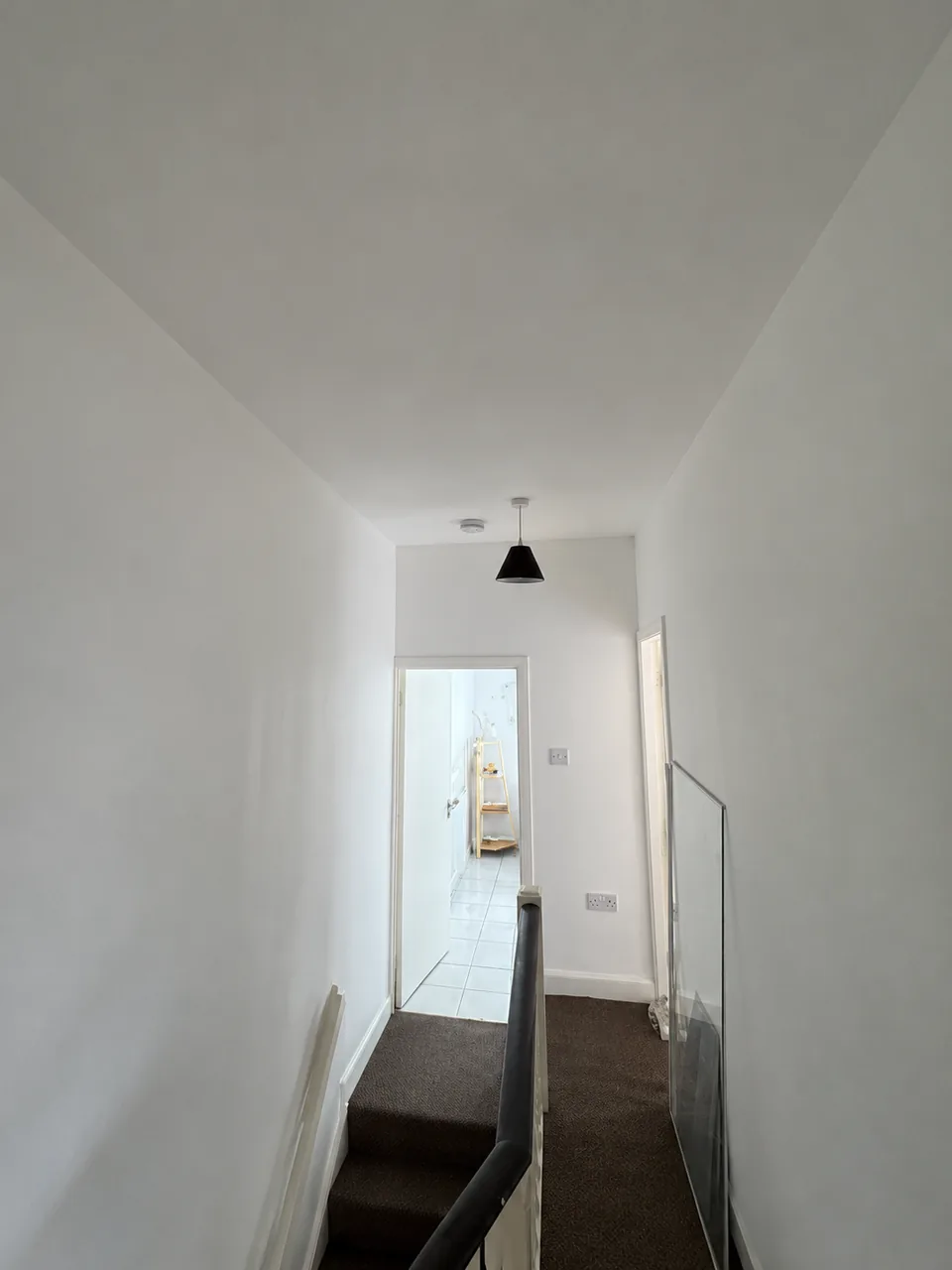 White-painted landing with white door frames and a dark handrail