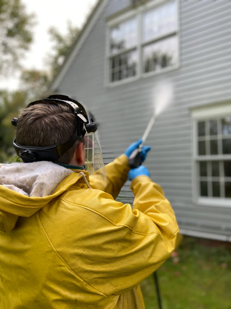 Person pressure washing the exterior of a house